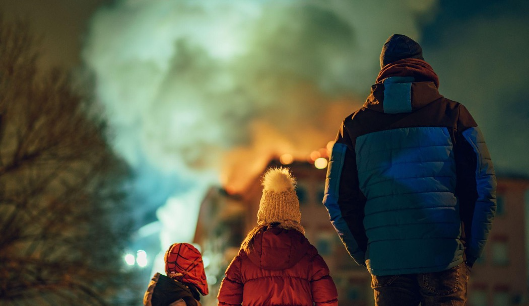 Three people facing a building on fire