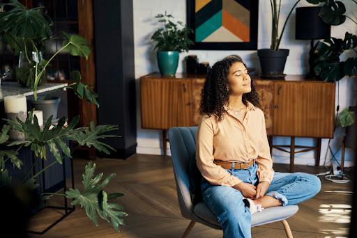 woman sitting on a chair in a room with eyes closed, with plants nearby