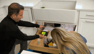 DryMedic technician inspecting water damage under a kitchen sink with a homeowner.